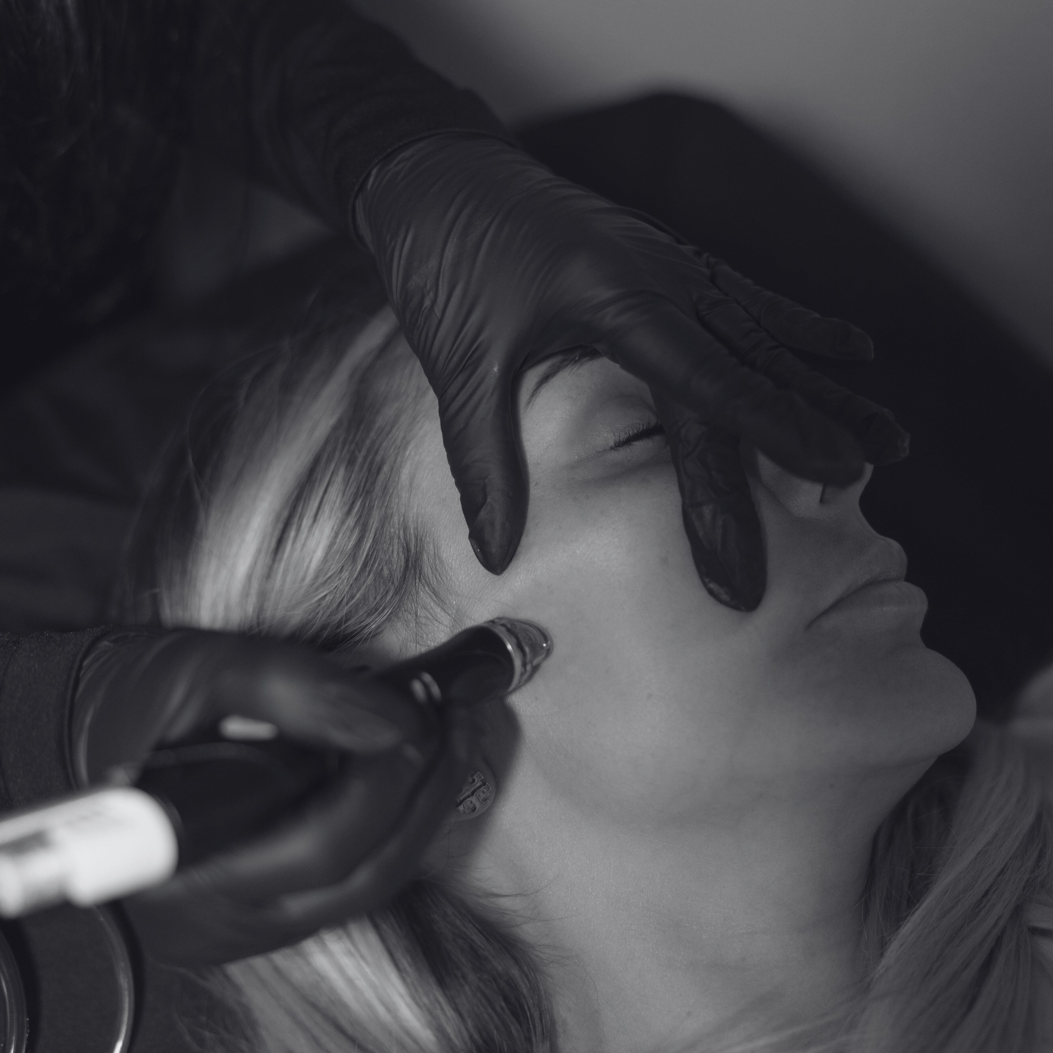 Person receiving a hair treatment with a gloved hand holding a tool.
