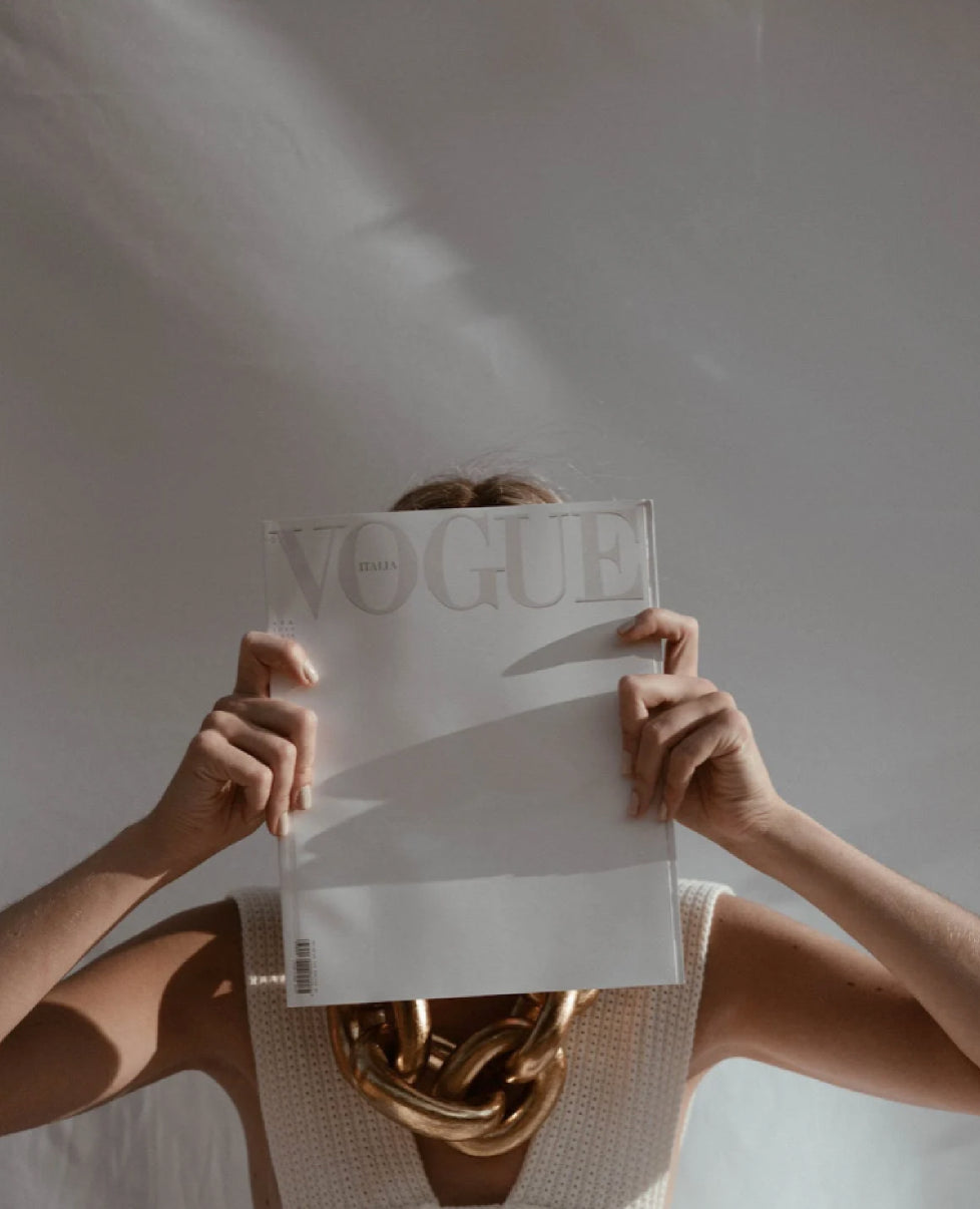 A woman holding a vogue magazine over her face.