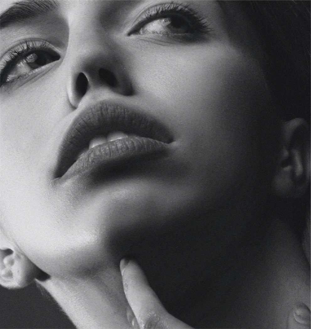 A zoomed in photo of a woman with her chin titled upward and her hand resting on her face.