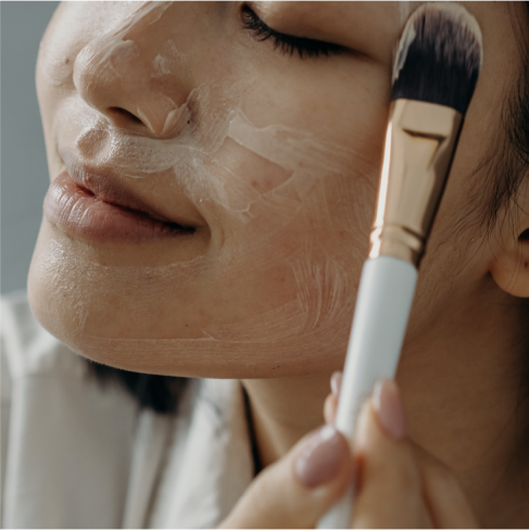 A woman applying skin care to her face with a makeup brush.