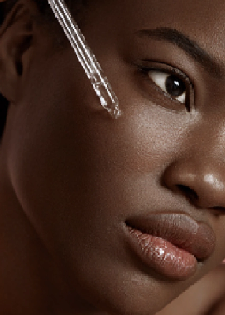 A woman using a dropper to apply skin care to her face.